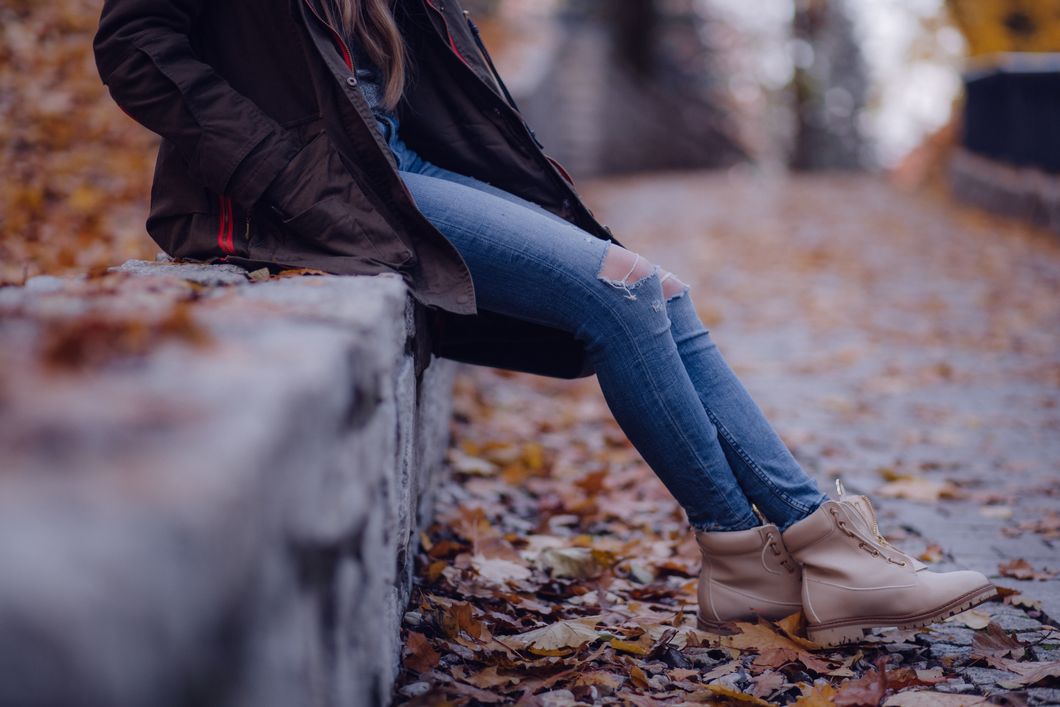 Girl wearing jeans and boots, sitting next to leaves