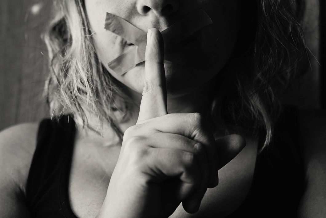girl with finger to lip and taped mouth