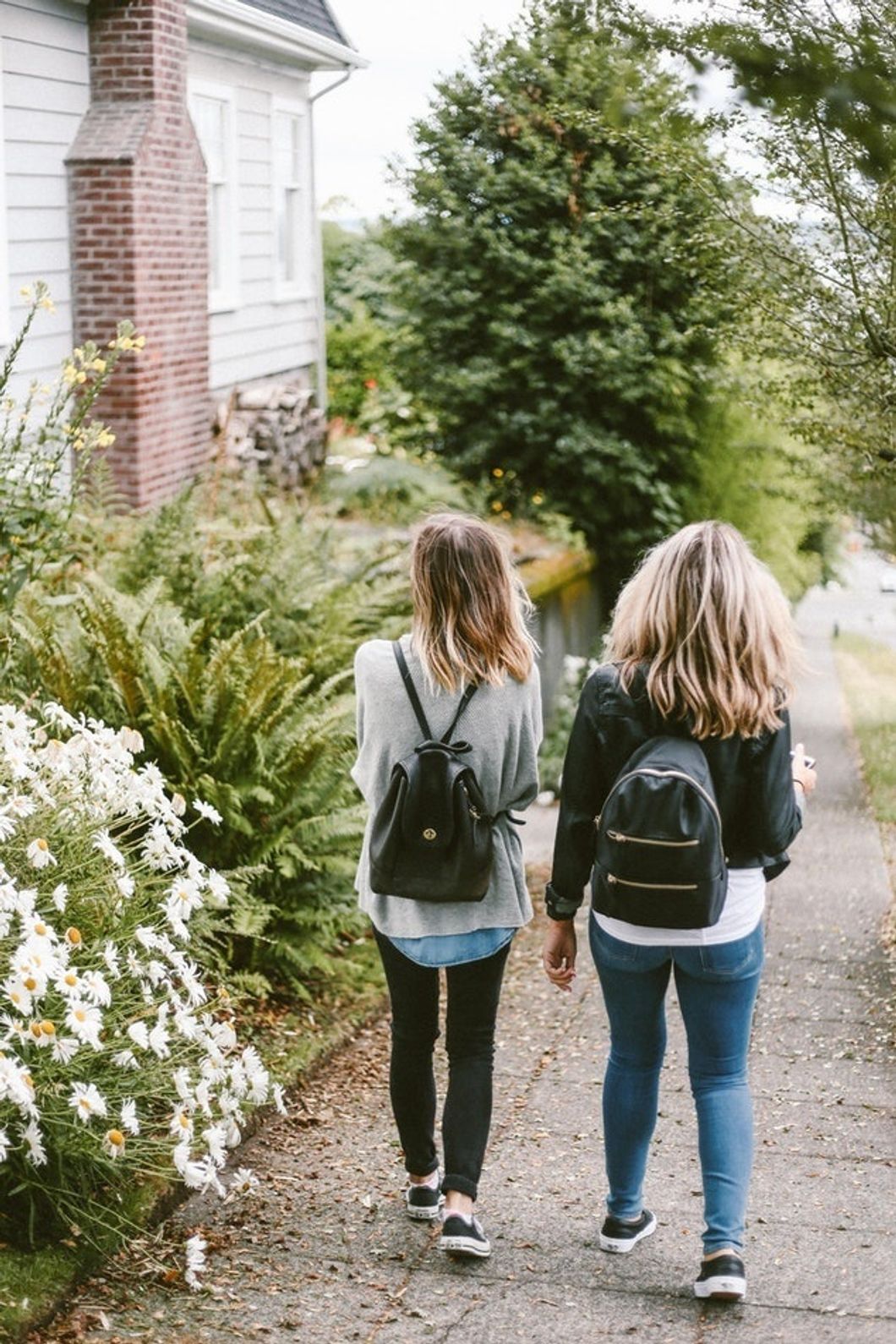 girls wearing backpacks walking down sidewalk together