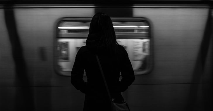 grayscale photography of woman standing near running train