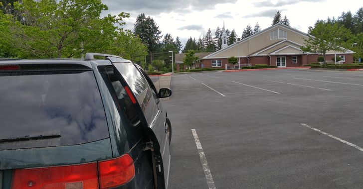 Green van with door open in parking lot with a church in the foreground