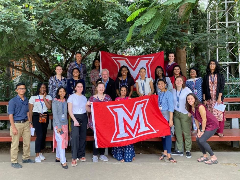 Group of students standing outside on bleachers with 2 "M" flags (for Miami University).