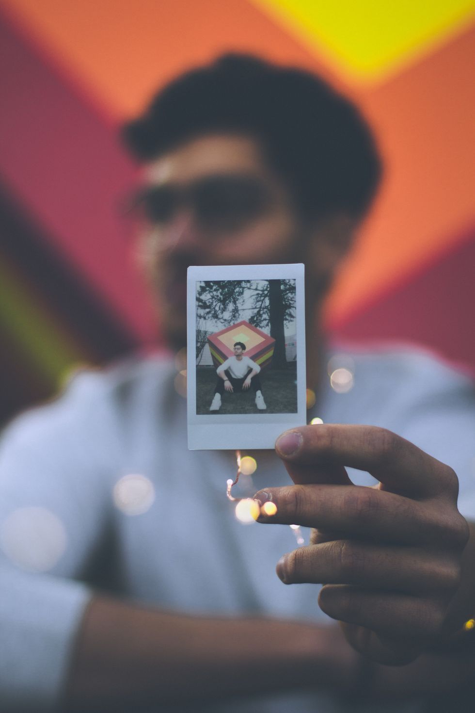 Guy holding up polaroid picture of himself against a colorful background