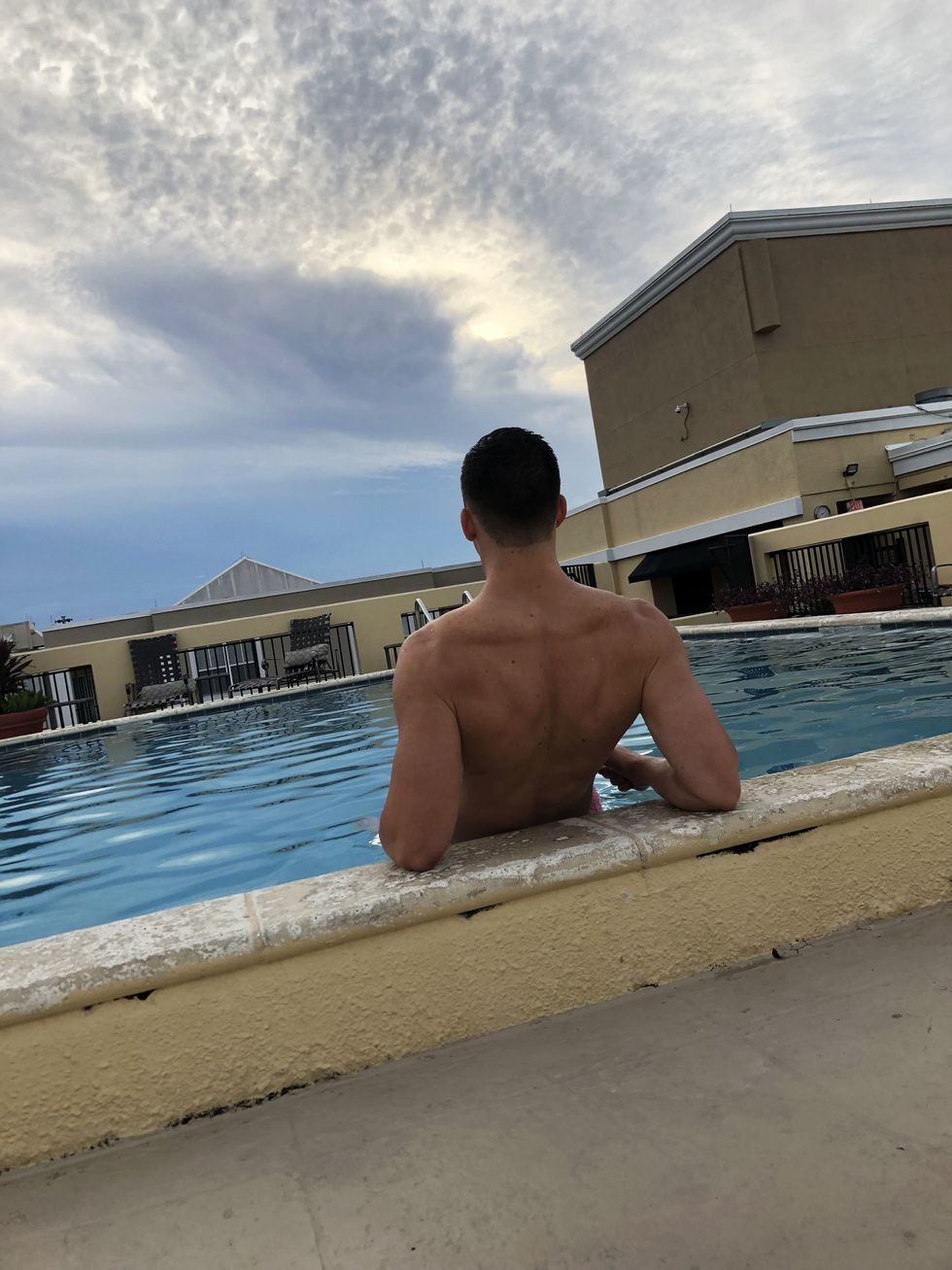 guy sitting with his back to the camera by the ledge of a pool