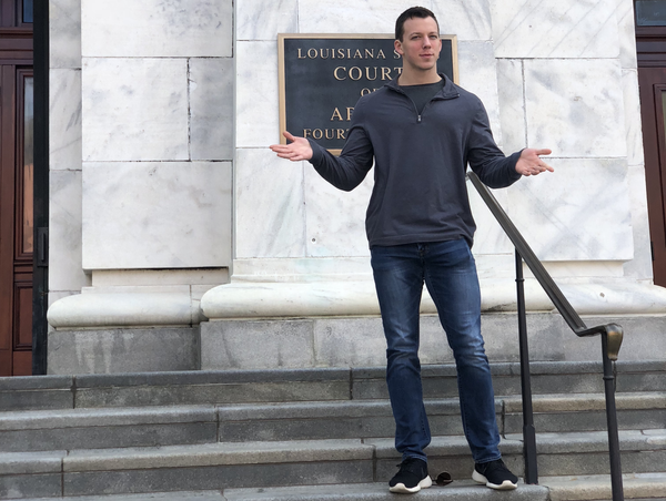 guy standing in front of a courthouse in New Orleans with his hands out in a questioning gesture