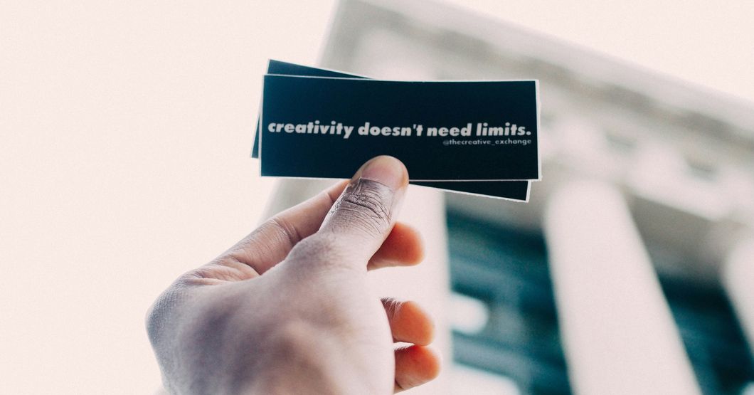 Hand holding black cards with white writing saying creativity does not need limits