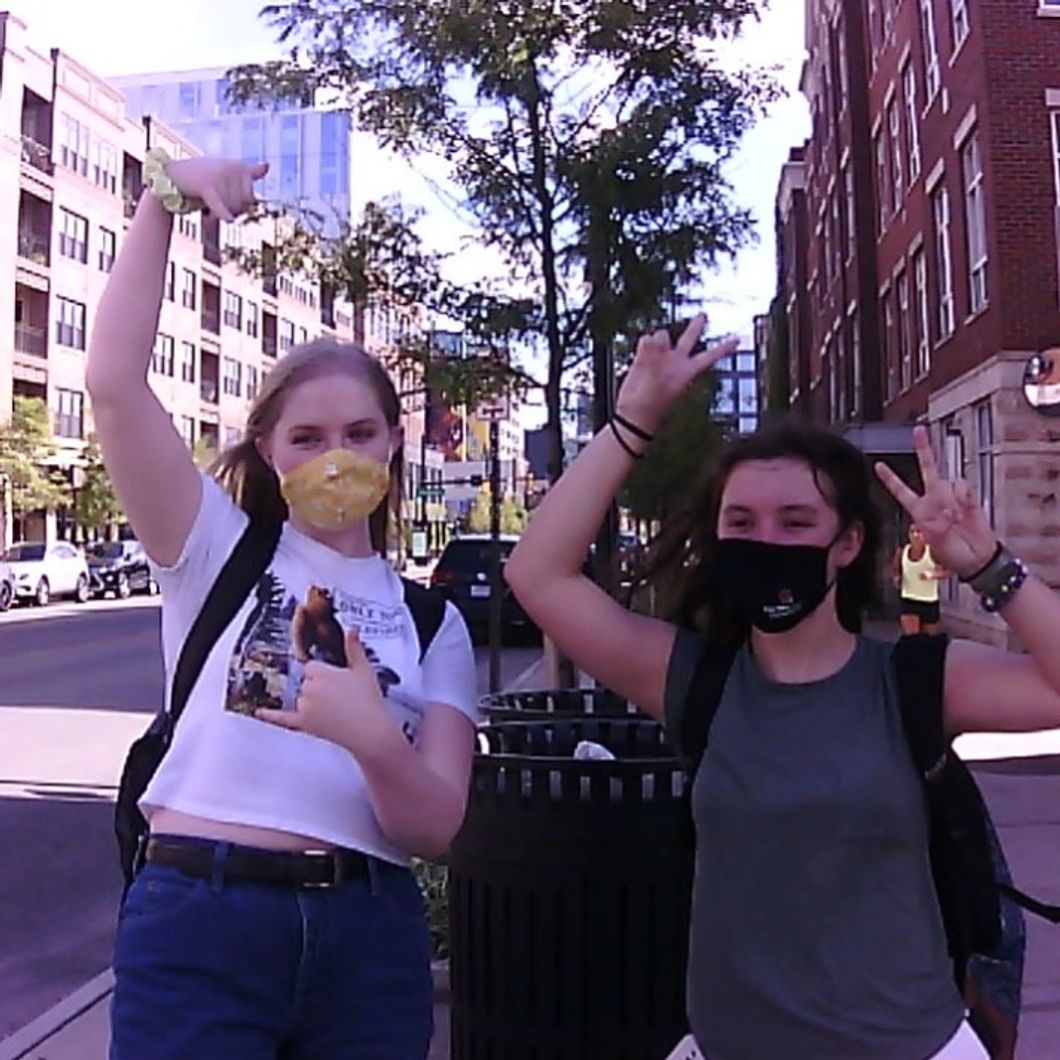 Hannah and Sarah pose happily, flashing peace signs, with The Short North in the background.