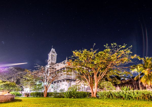 House of wonders building at night with trees and grass in stone town