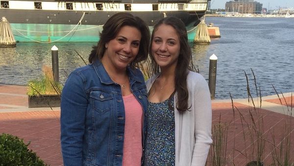 Jenna Pizzi and her mom smiling by a waterfront with a historic ship in the background.