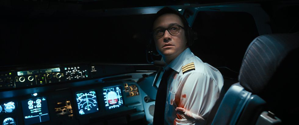 Joseph Gordon-Levitt is pictured as Tobias Ellis in Amazon Prime's "7500." His arm left arm is bloodied and wrapped with a bandage. He's turning the upper half of his body up toward a screen he's watching in the plane's cockpit.