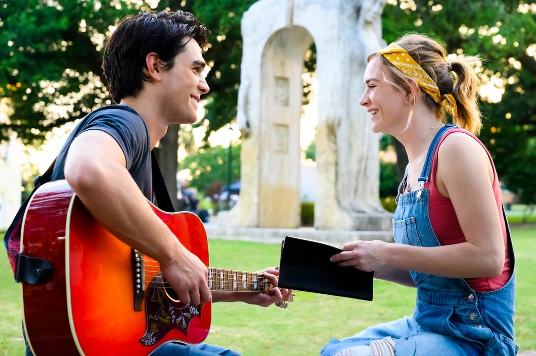 K.J. Apa playing Christian music star Jeremy Camp and Britt Robertson playing Melissa Henning star in "I Still Believe." Apa is playing a guitar while Robertson is holding a journal, both of them smiling at each other.