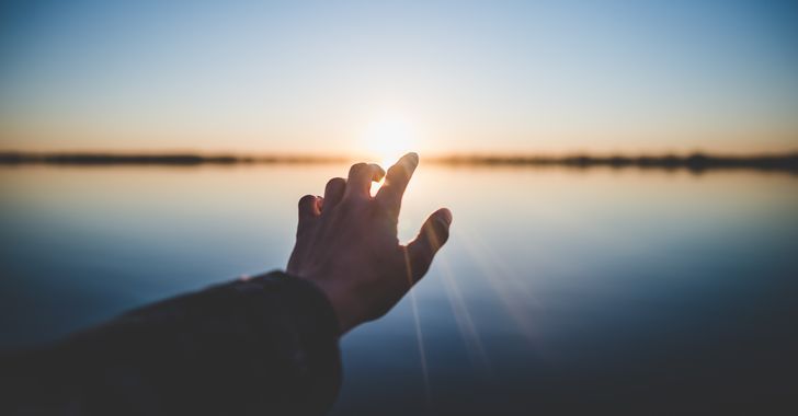 Landscape photography of person's hand in front of sun
