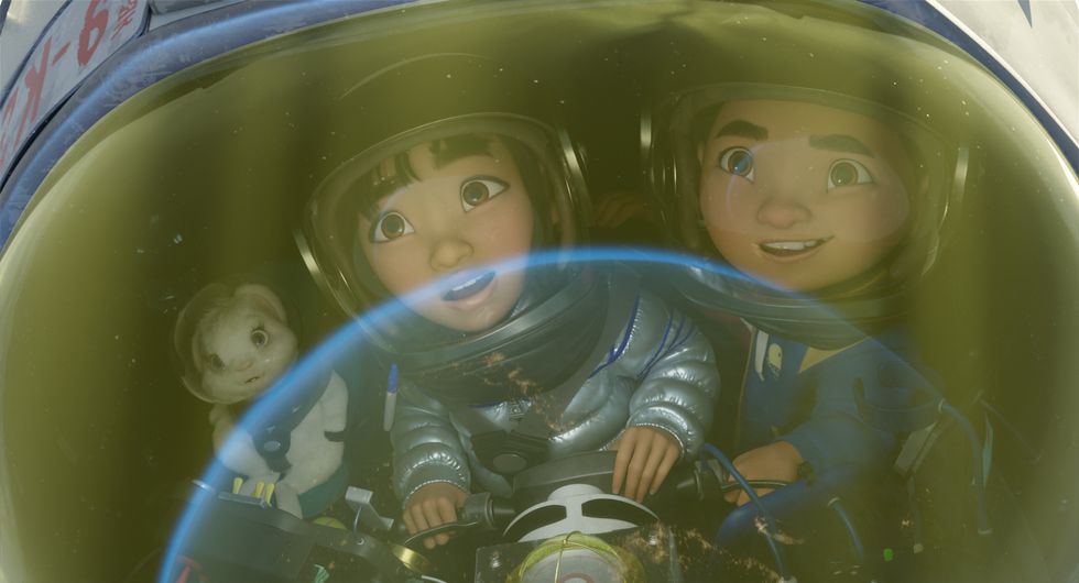 (Left to right) Pet rabbit Bungee, main character Fei Fei and her soon-to-be brother Chin are in a small, handmade space ship. They're all staring in awe of a beam of light that's carrying them toward space. They're all wearing astronaut helmets, with Fei Fei specifically in a homemade space suit. The film still image is a tight shot.