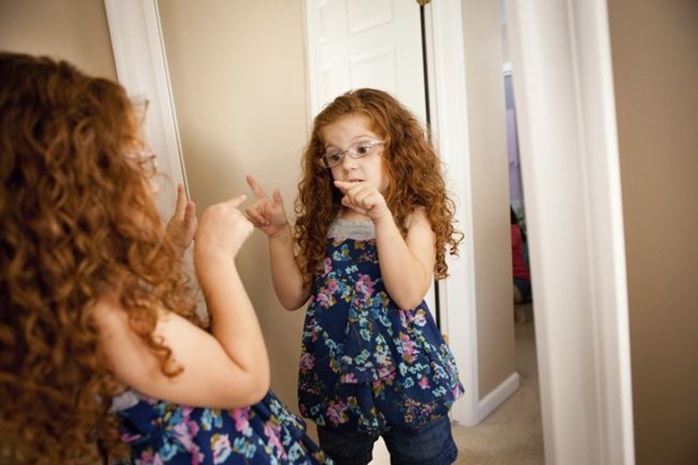 Little girl pointing her fingers at her reflection in the mirror. 