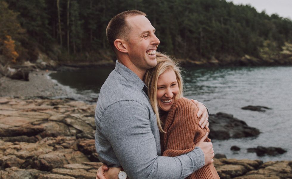 Man and woman hugging and laughing while looking out at a lake