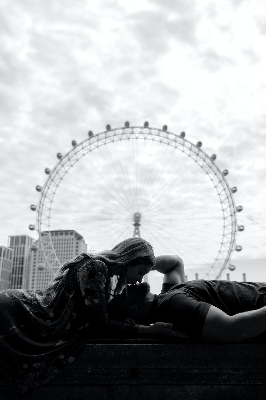 Man and woman laying down infront of the london eye kissing