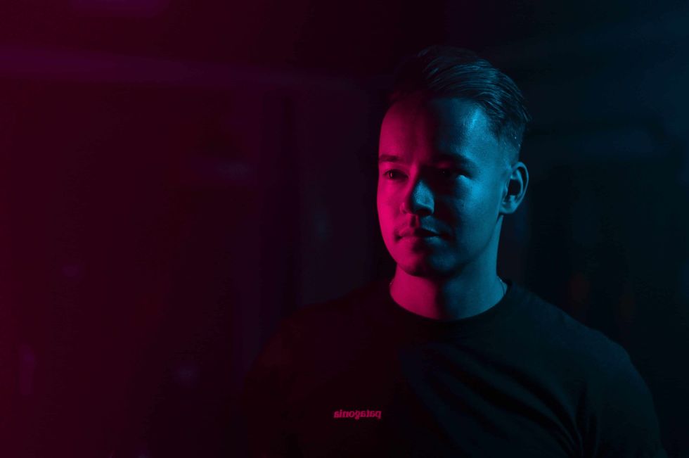 Man half-lit in red and blue light, standing in a dark, moody setting.
