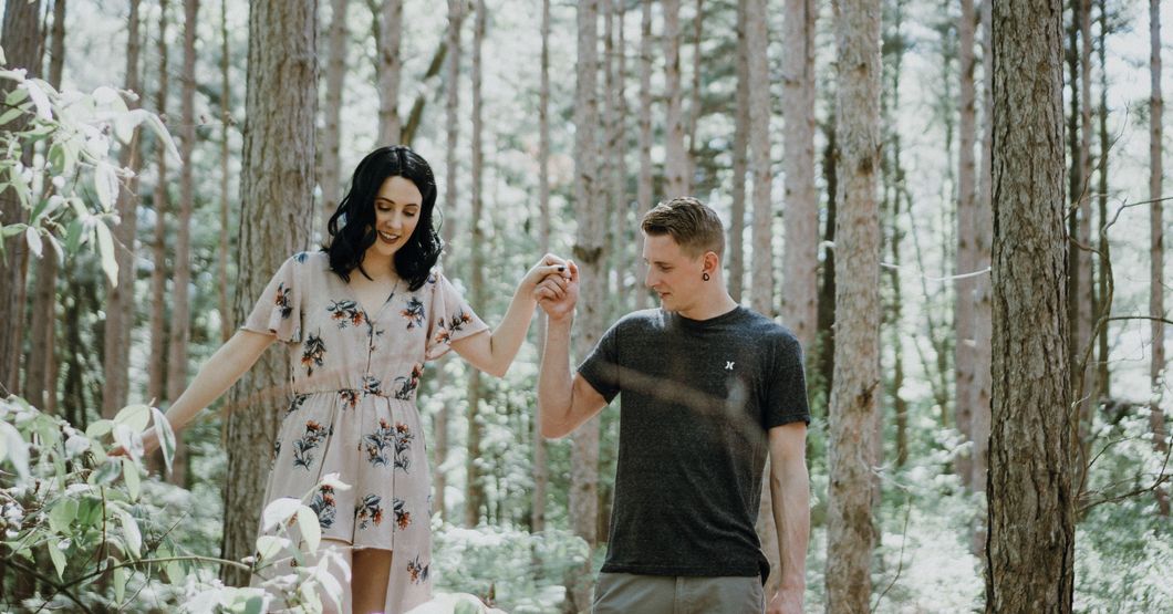 Man holding womans hand walking through a forrest