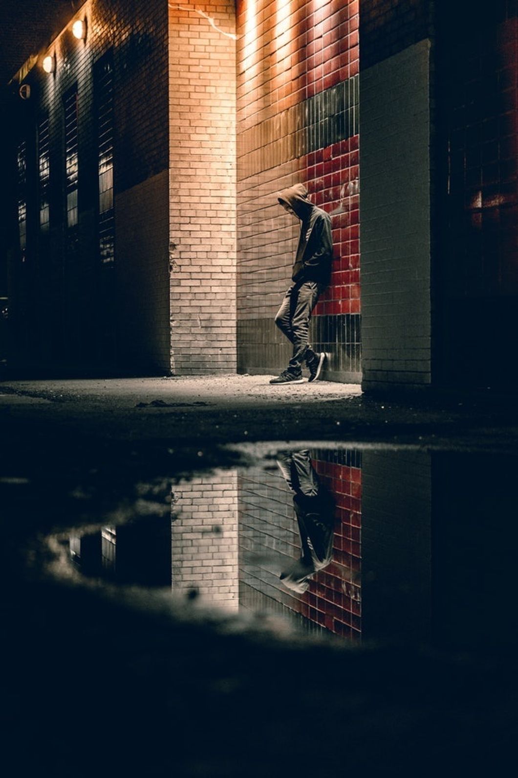 man in hood standing against brick wall in alleyway