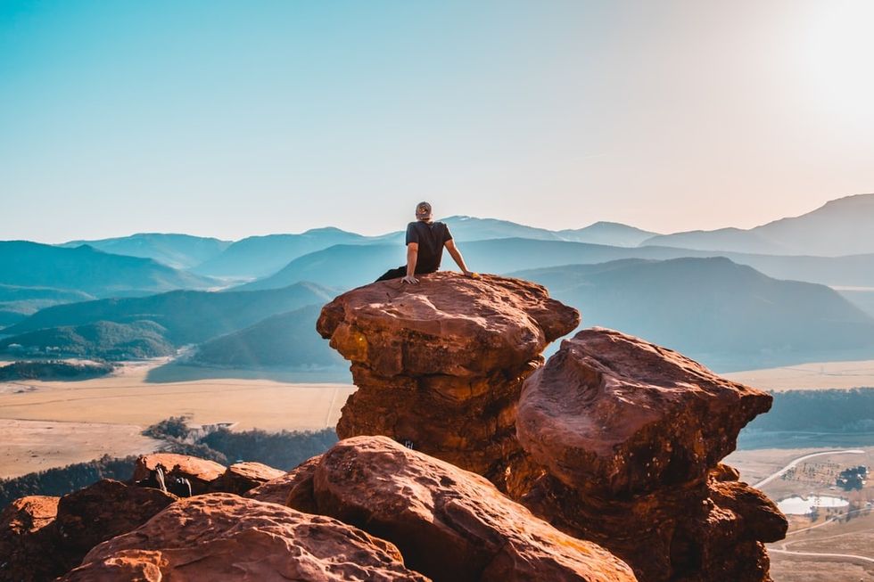 Man sitting on a large rock formation and staring out into the rocky landscape