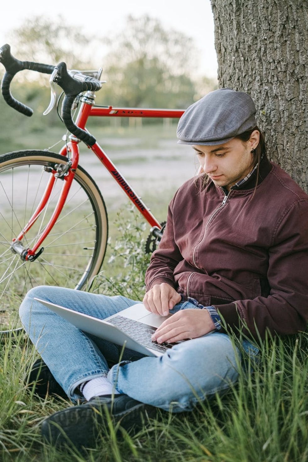 man sitting under a tree with his laptop and bike in the background.