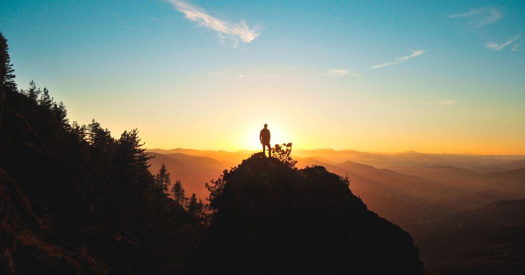 man stands on mountain top at sunset