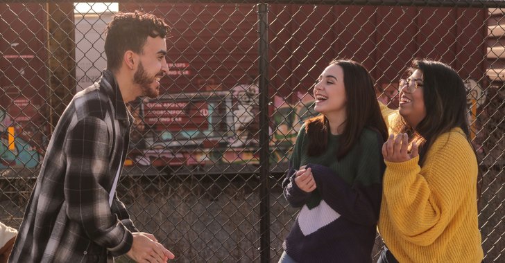 man talking to two women laughing at him near fence