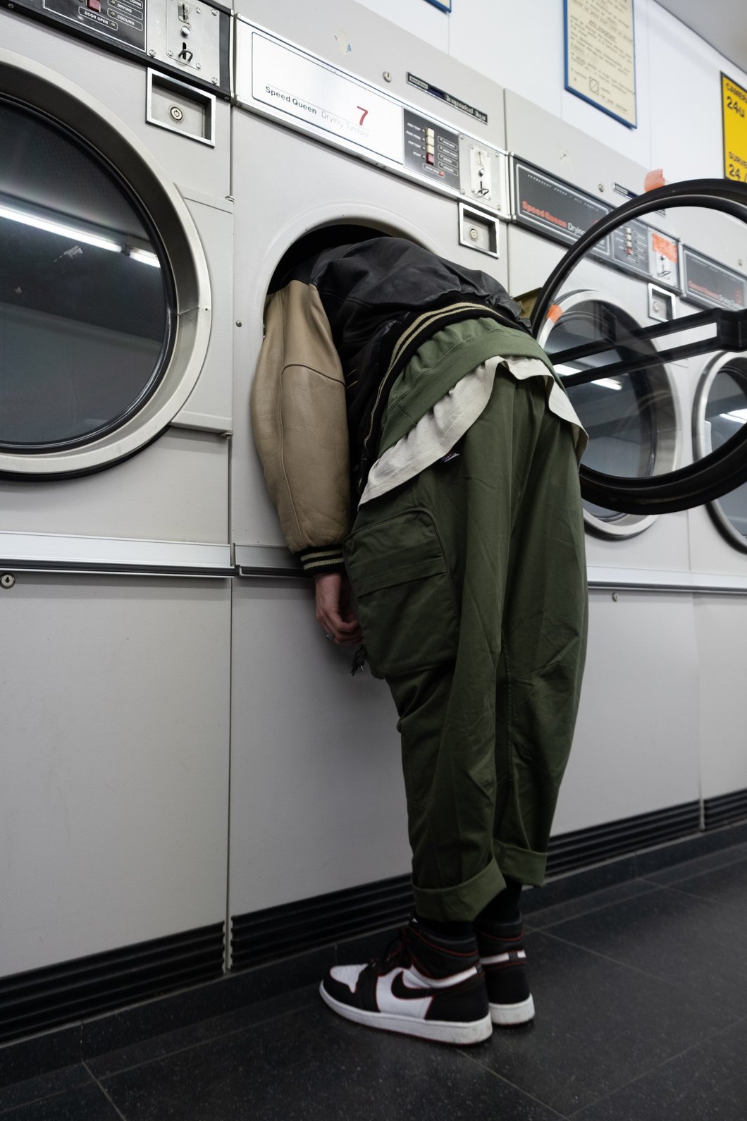 Man with a reen jacket with head inside a white front load washing machine