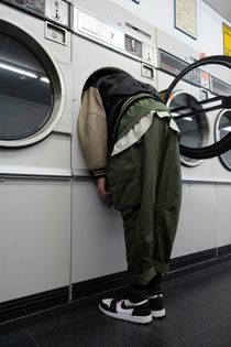 Man with a reen jacket with head inside a white front load washing machine