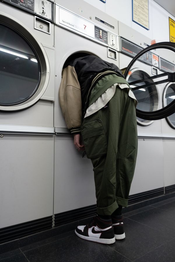 Man with a reen jacket with head inside a white front load washing machine