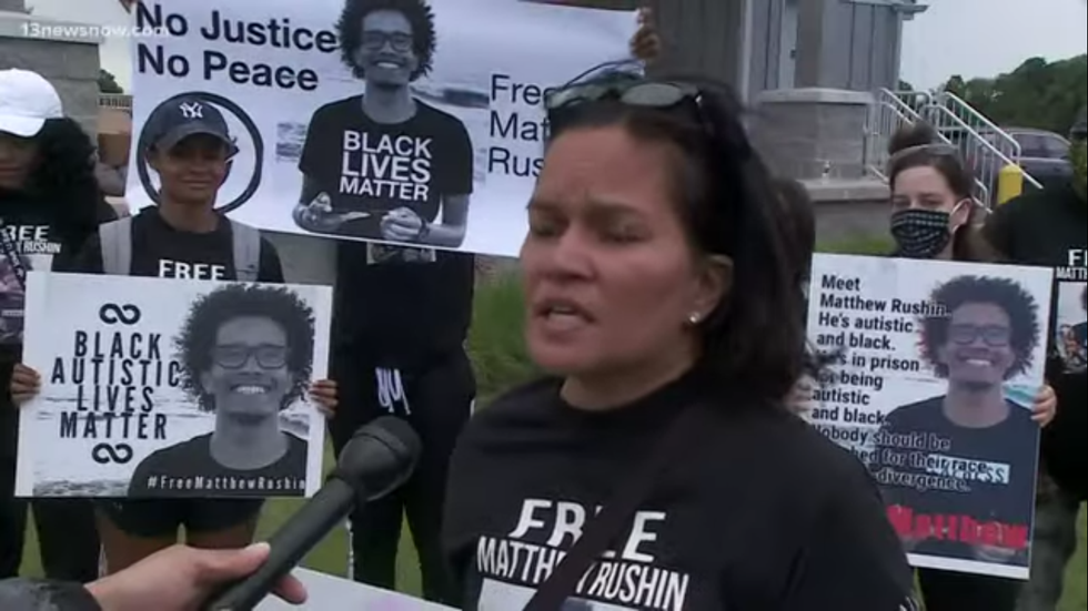Matthew Rushins mother speaks to the crowd during a protest people are in the background holding signs that say "Free Matthew Rushin" and "Black Autistic Lives Matter"