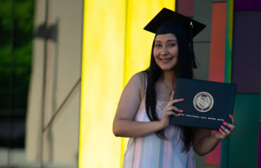 me holding a picture of my diploma with a graduation hat on 
