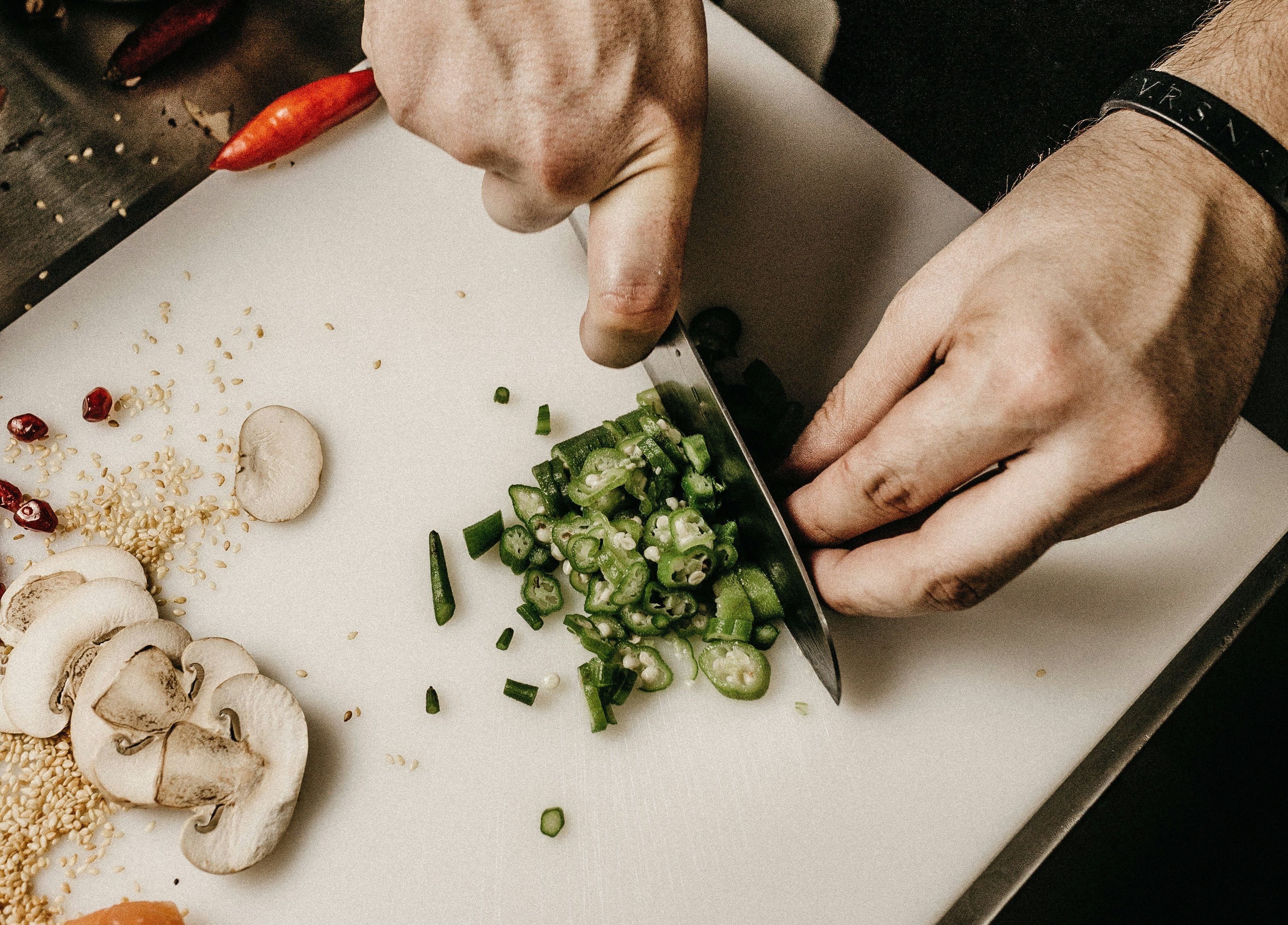 Person chopping green vegetables on a cutting board with mushrooms and salmon nearby.