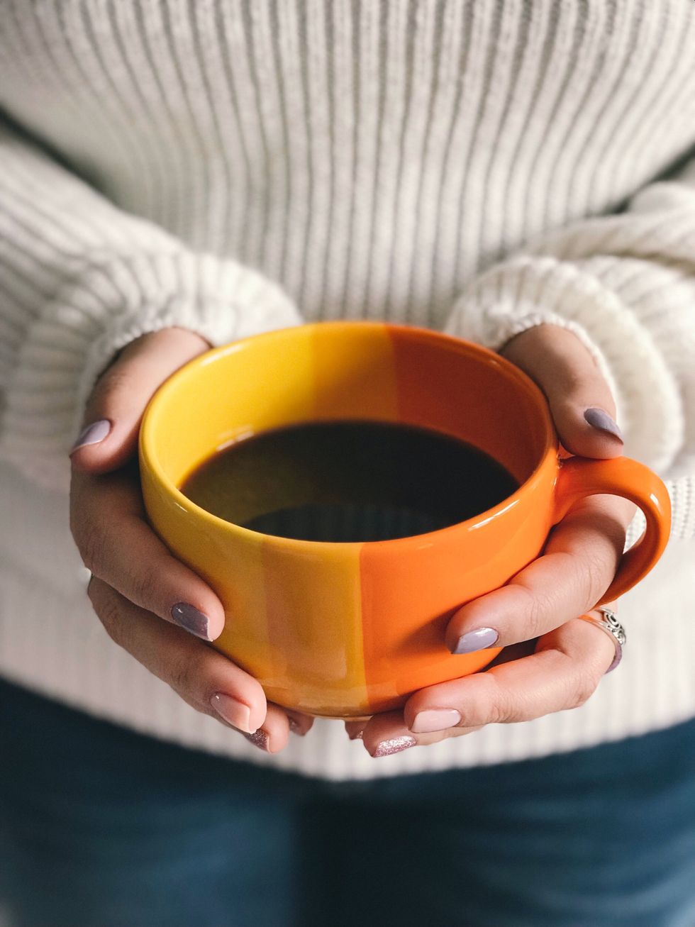 person holding orange cup filled with dark brown color liquid