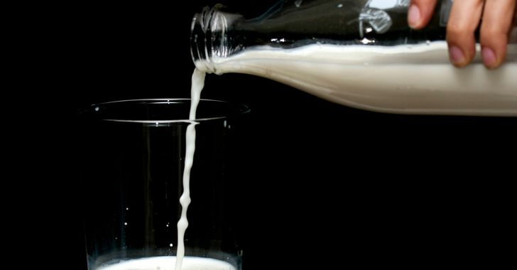 person pouring milk on clear drinking glass