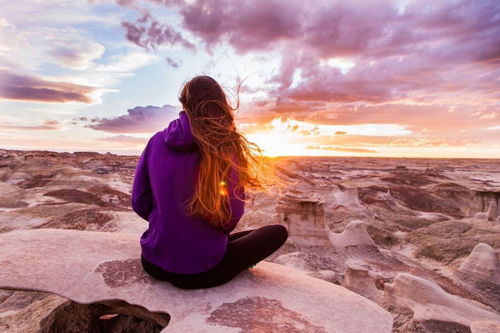 Person sitting on a rock overlooking a desert landscape at sunset.