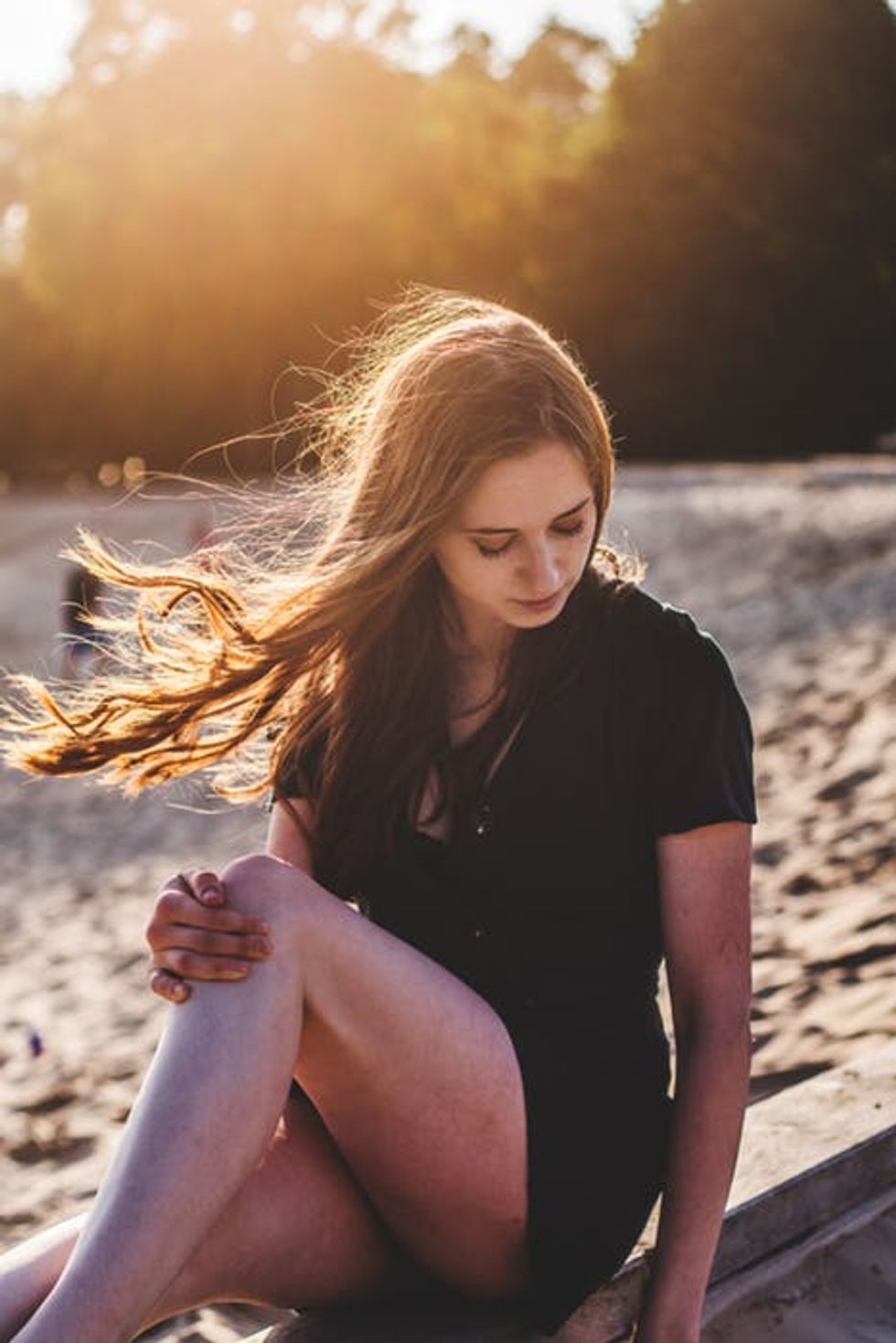 Person sitting on the beach with hair blowing in the wind.