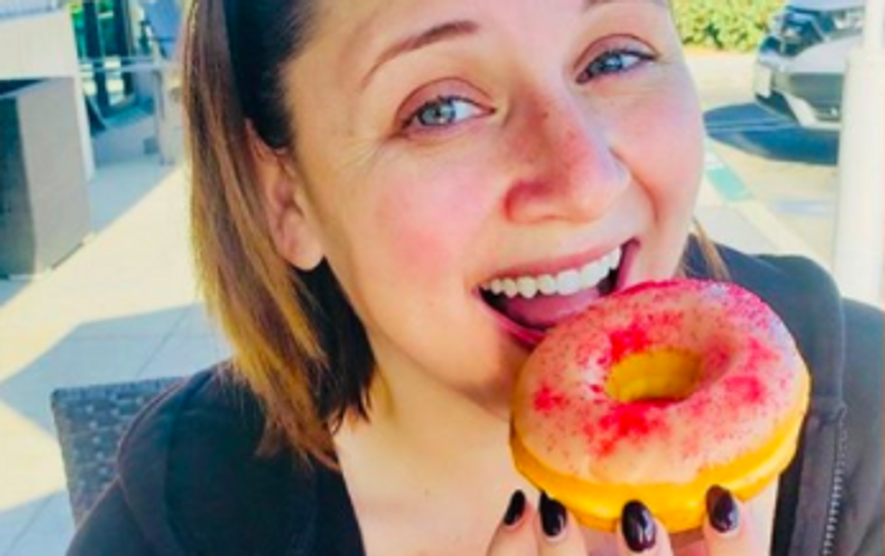 person smiling as they get ready to bite in to donut with white and red frosting