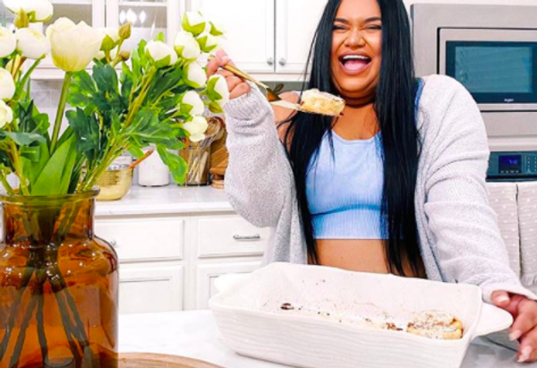 person smiling in kitchen eating cinnamon rolls with pan full of them on kitchen counter