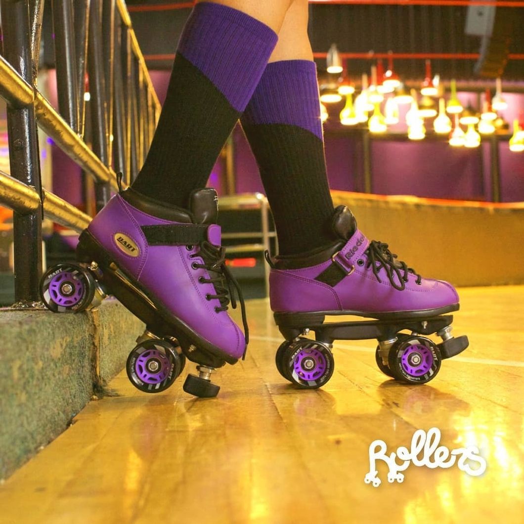 person standing in purple roller skates at rink