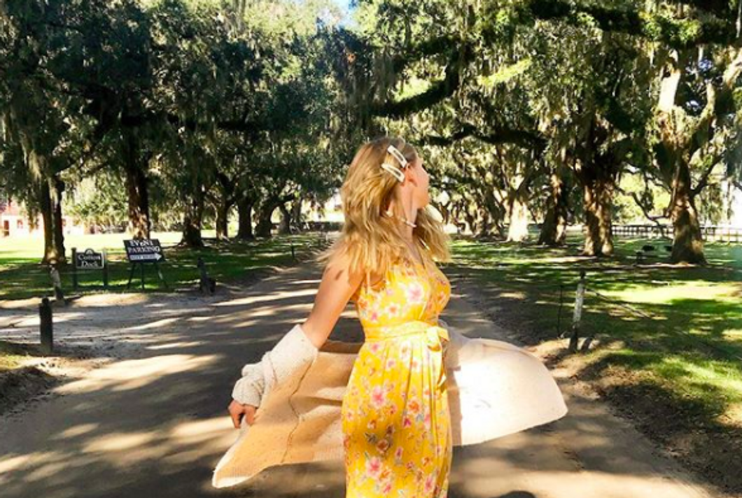 person wearing dress and sweater, spinning on a sidewalk with trees behind them