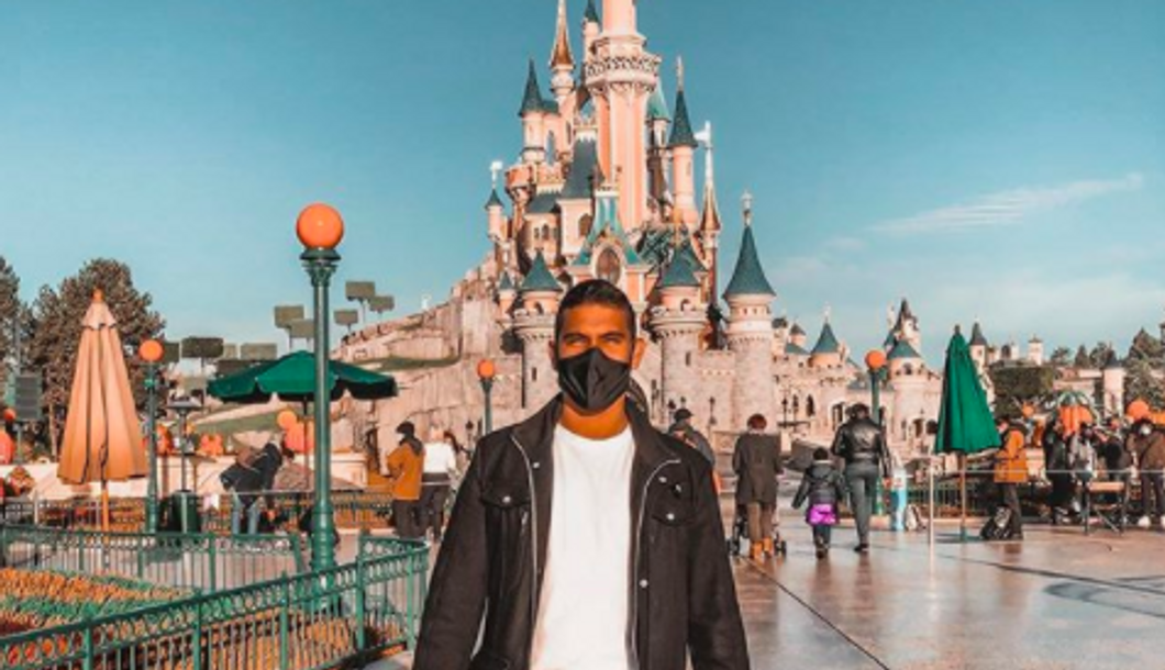 person wearing mask standing in front of the Disney castle