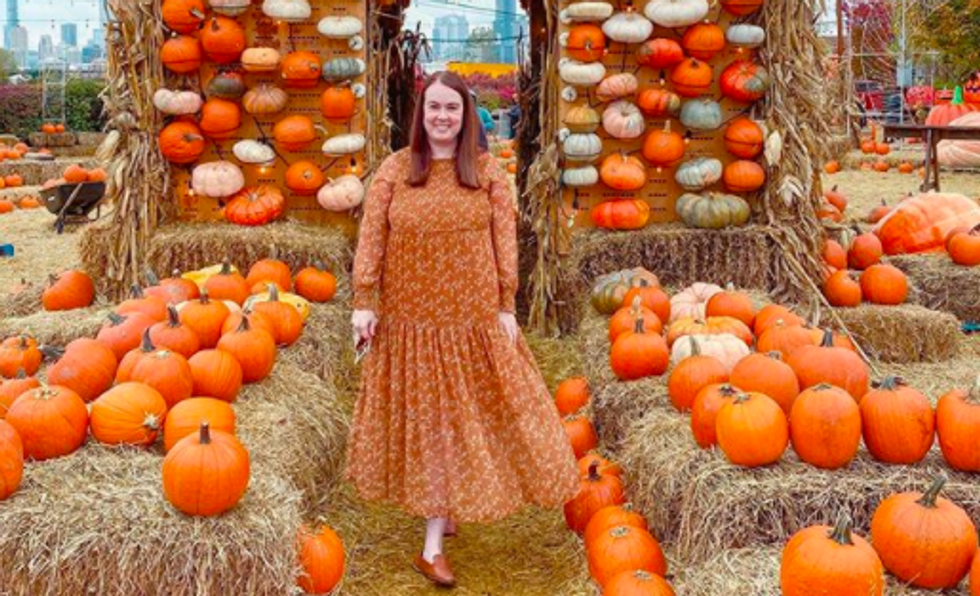 person wearing orange dress standing in front of hay and pumpkins