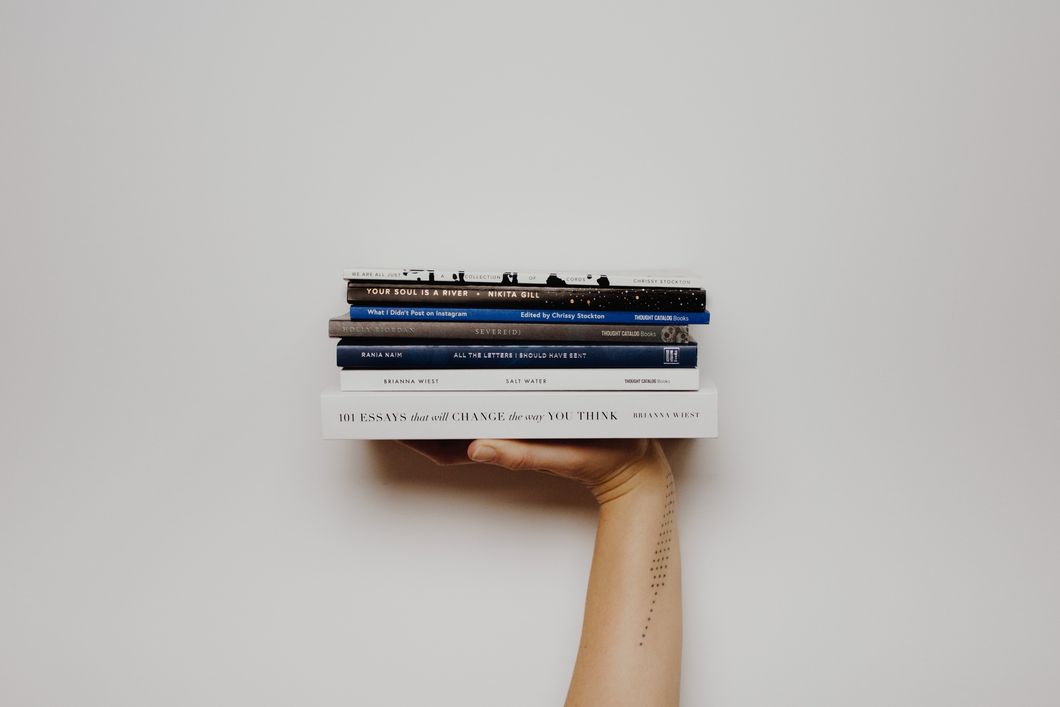 person with a tattoo holding a small stack of books