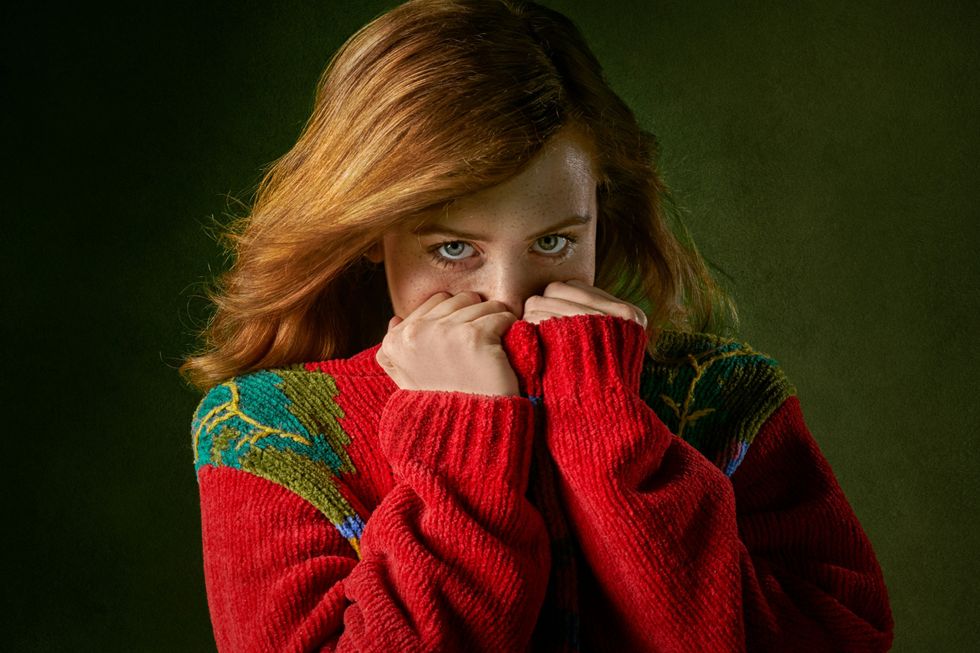 Person with red hair peeking over their red sweater in front of a dark green background.