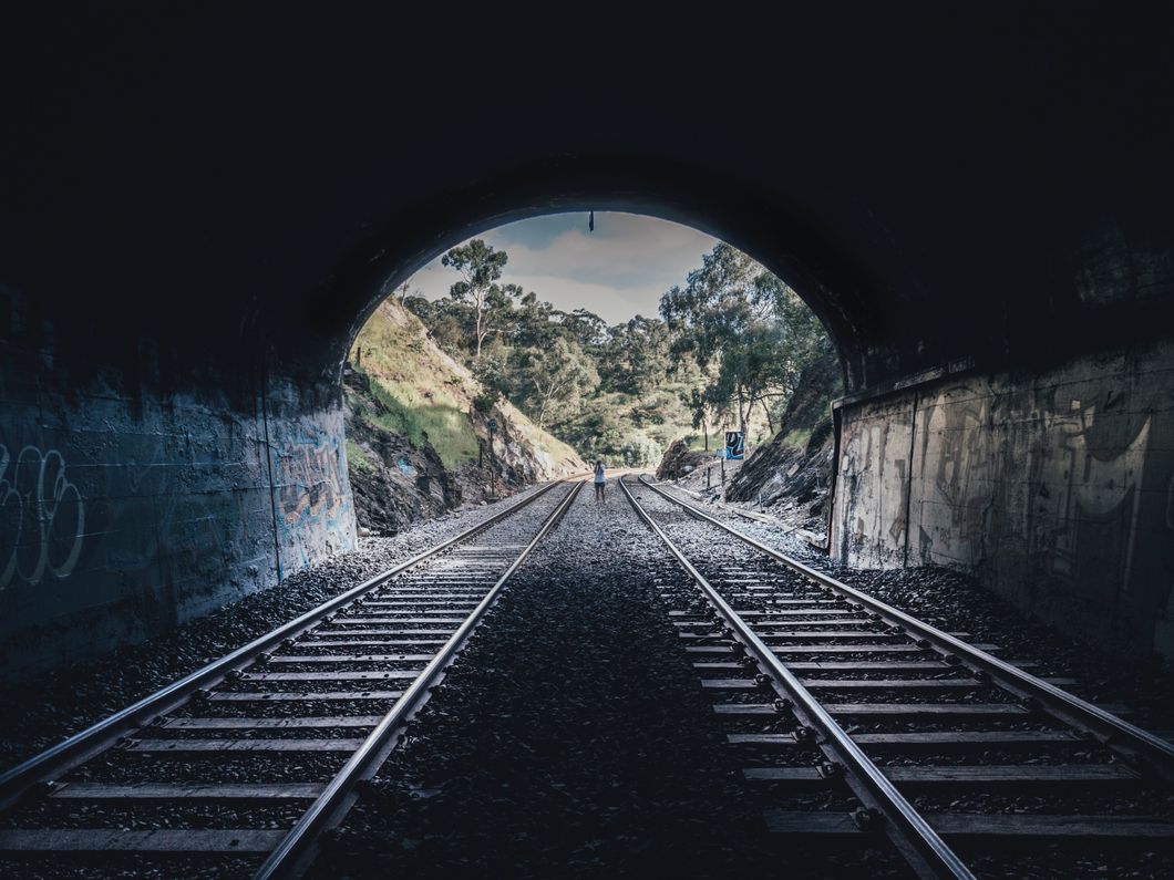 Railroad tracks going through a tunnel with one person standing in the middle with their back to the camera.