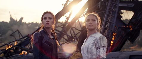 Scarlett Johansson (left) as Black Widow and Florence Pugh (right) as Natasha's sister Yelena Belova look past the camera in a movie still from "Black Widow." The sisters seem to have survived a calamity as there is lots of wreckage and metal bars in the background.