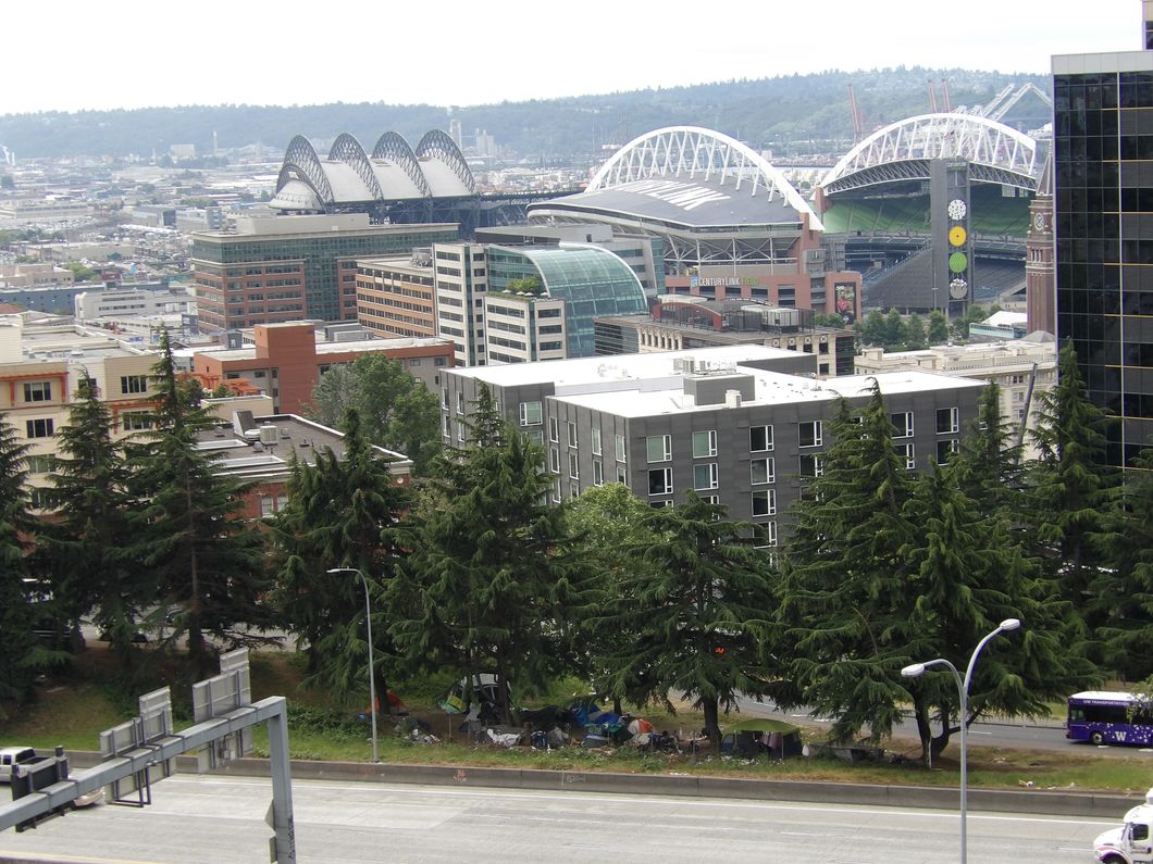 Seattle between CenturyLink Stadium and Interstate 5, including a strip of greenscaped land with large evergreen trees next to the interstate with tents and clutter under the trees