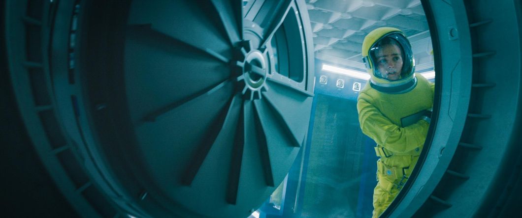 Sela looks outside of an air duct on a spaceship in sci-fi thriller "Voyagers." Actor Lily-Rose Depp is wearing a bright yellow hazmat suit while peeking outside the air duct that opens to space.