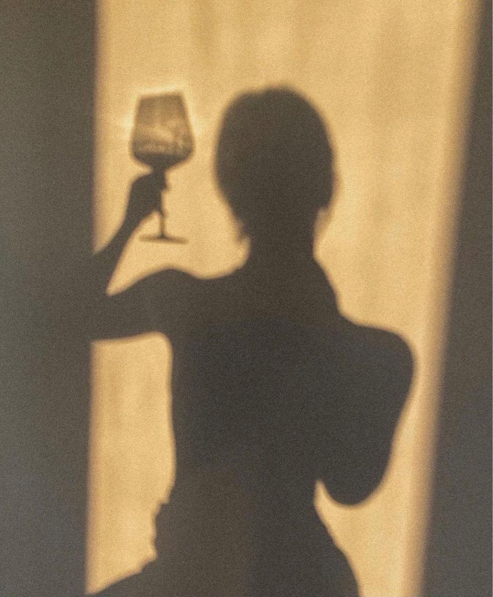Shadow of a happy single girl sipping on a glass of wine.
